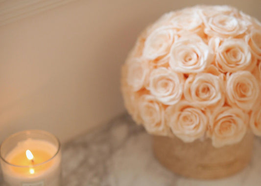 In a natural travertine container, beige eternal roses are neatly arranged, with a candle flickering beside them, adding a warm and romantic atmosphere to your home.