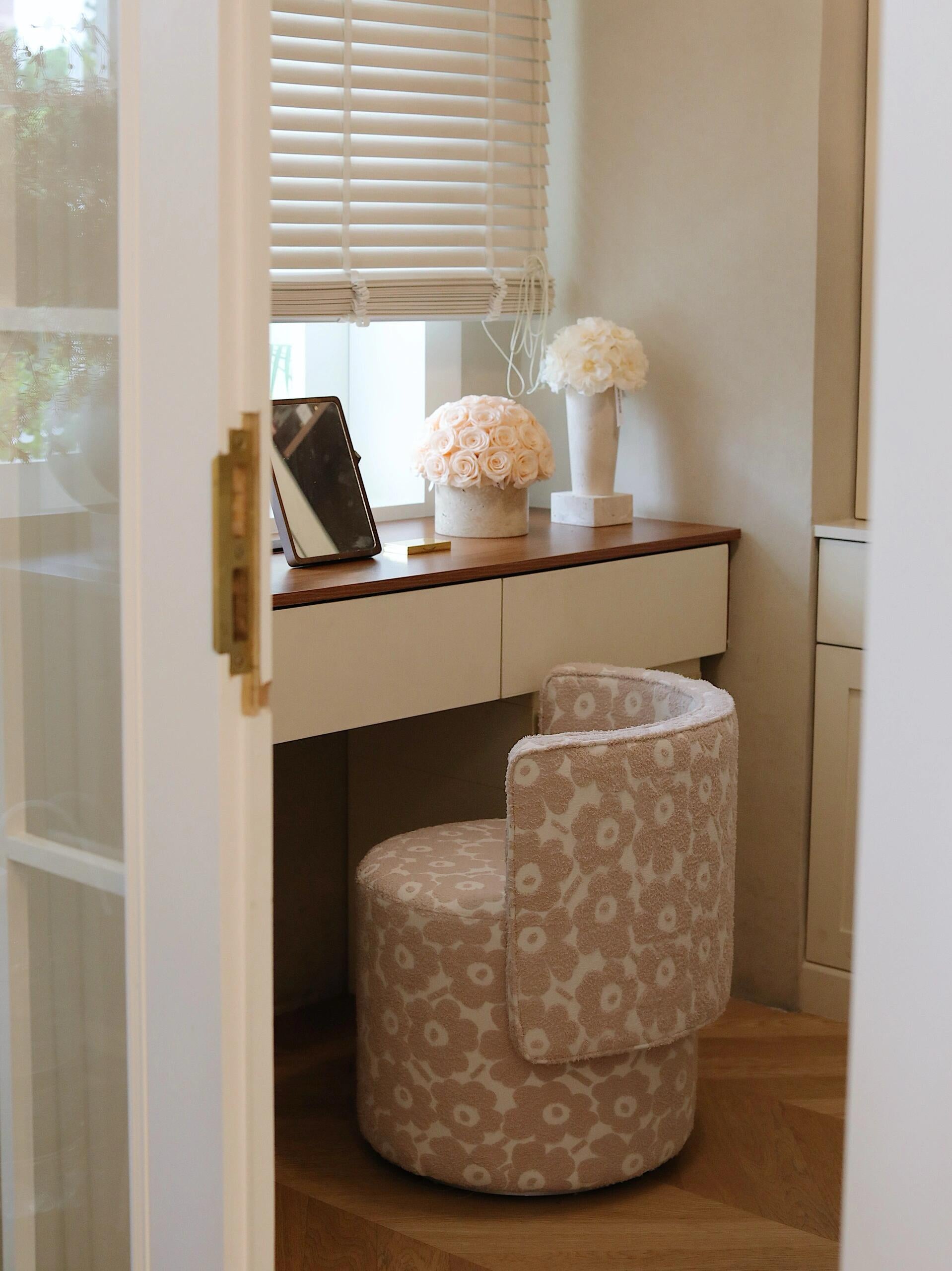 
A window-side desk paired with a patterned chair. On the desk, there are two floral arrangements, including a pot of beige eternal roses, bringing a touch of nature and elegance to the space.