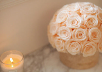 In a natural travertine container, beige eternal roses are neatly arranged, with a candle flickering beside them, adding a warm and romantic atmosphere to your home.