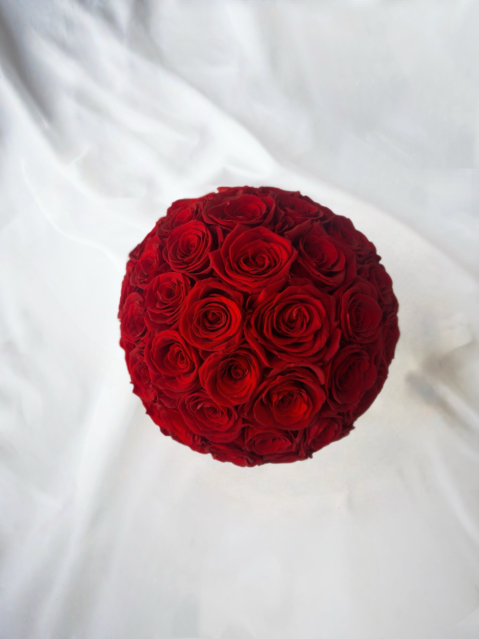 A spherical bouquet of vivid red preserved roses, arranged densely to form a perfect round shape. Set against a soft white backdrop, it showcases an intense and lasting beauty, ideal for adding a touch of elegance and romance to any space.
