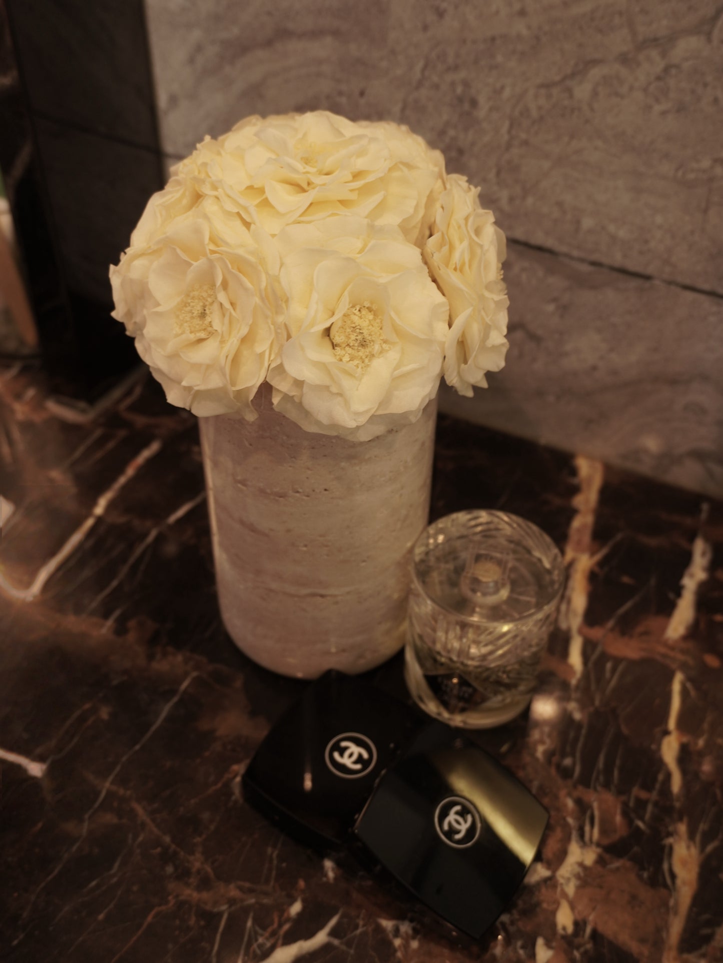 
A travertine vase with a bouquet of white preserved roses sits on a luxurious marble surface. Next to it are a delicate glass and a high - end perfume bottle, creating an elegant and refined decor display.
